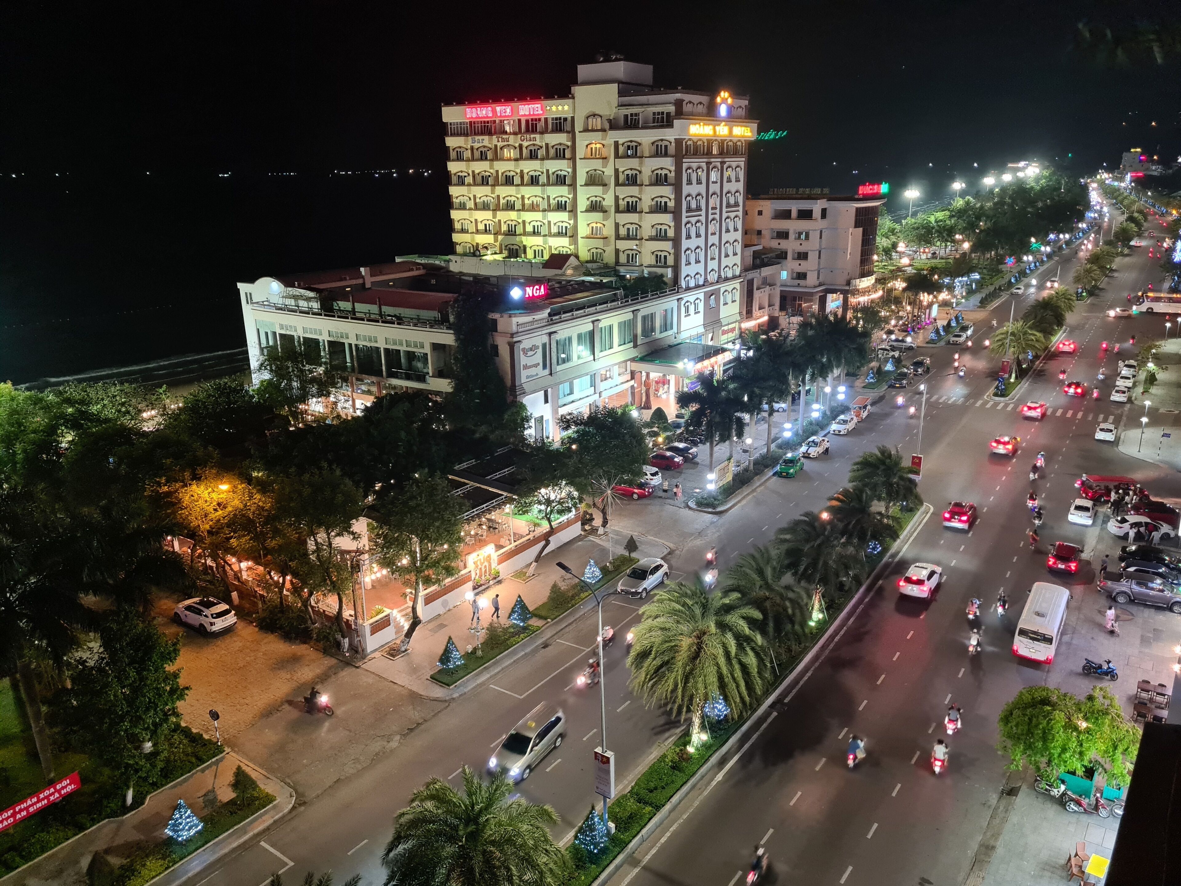 Un hotel de varios pisos con bar y restaurante en la planta baja, un estacionamiento y una calle concurrida con vehículos y peatones.