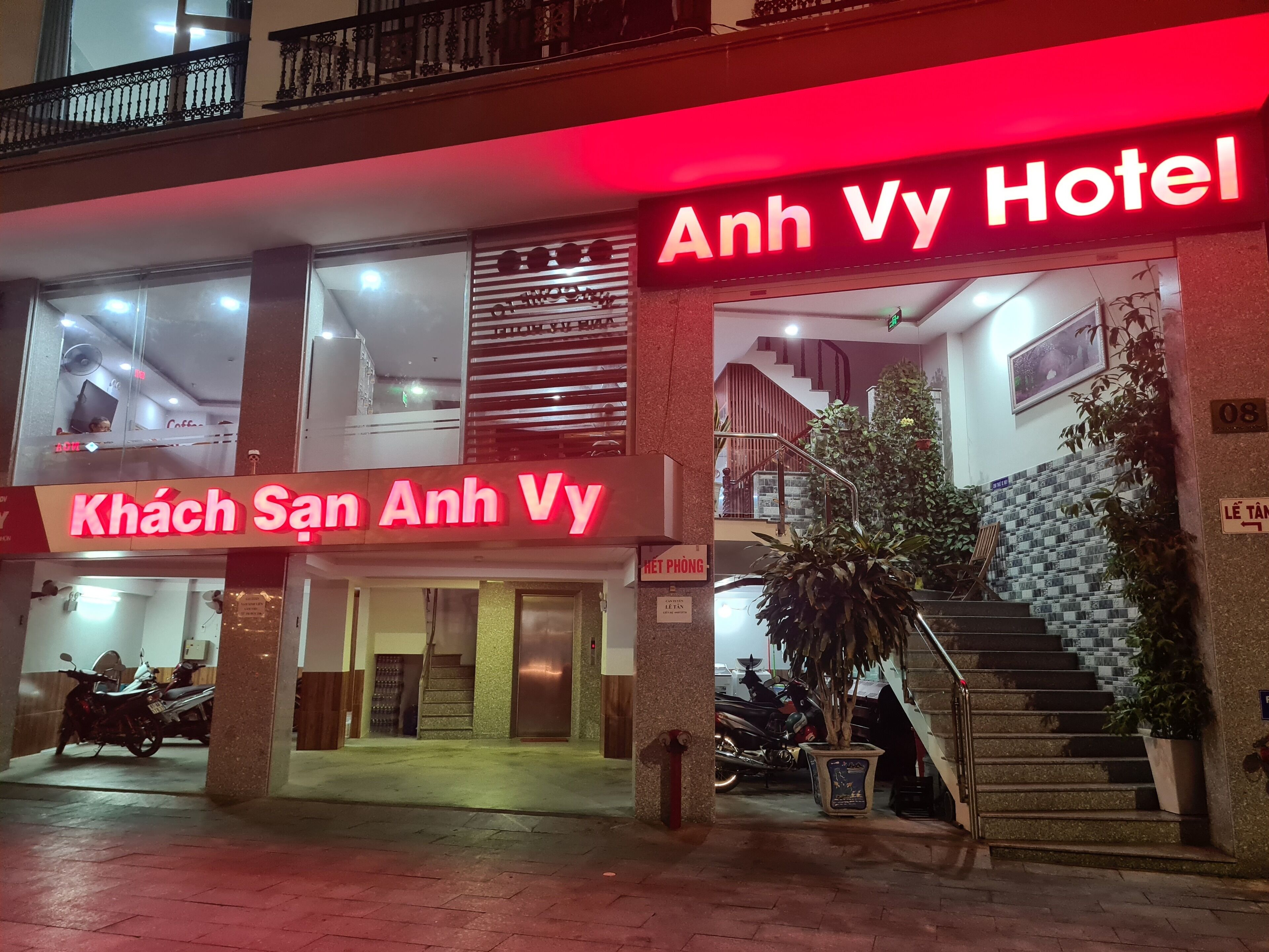 A hotel entrance with a staircase leading to the second floor, a signboard with hotel name, and a visible coffee shop sign.