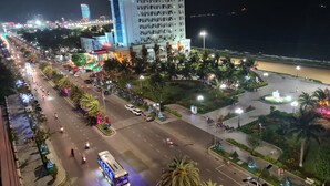 A multi-story hotel with a bar and cafe on the top floor, surrounded by palm trees and a well-lit street. - Anh Vy Hotel (Quy Nhon Nam)