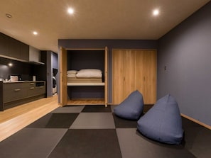 Ein kleines Schlafzimmer mit Bett, Kleiderschrank, einer kleinen Küchenzeile und einer Sitzecke mit Kissen.