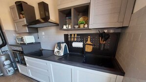 Een compacte keuken met witte kastjes, een zwart aanrecht, een broodrooster, een waterkoker en een fornuis.