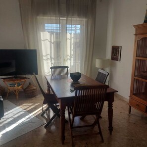 Uma sala de jantar com mesa de madeira, cadeiras, televisão e um armário.