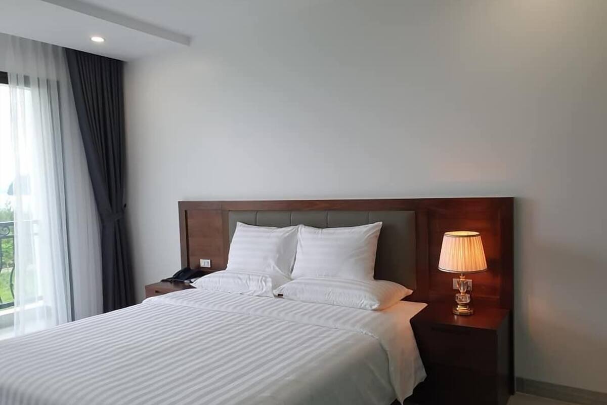 A hotel room with a large bed, a nightstand with a lamp, and a window with curtains.