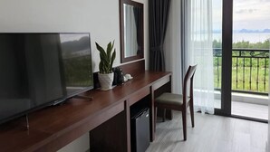 Una camera d'albergo moderna con una grande televisione a schermo piatto, una scrivania in legno, una sedia, una pianta in vaso, uno specchio e un balcone con vista sul mare.