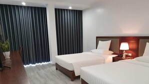 Camera d'albergo con due letti, una scrivania e una lampada.