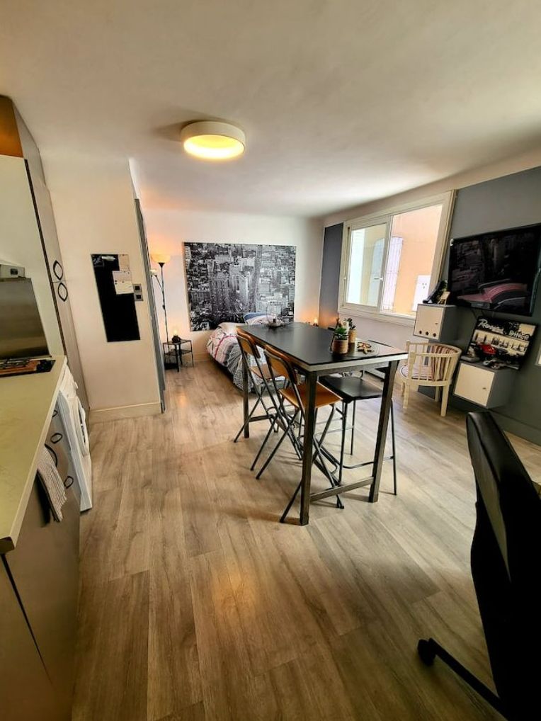 Eine kompakte Küche mit Essbereich, einem großen Fenster und einem Stadtbildgemälde.