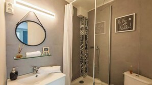 Un baño moderno con un espejo redondo, un lavabo blanco, una cabina de ducha de vidrio y un inodoro.
