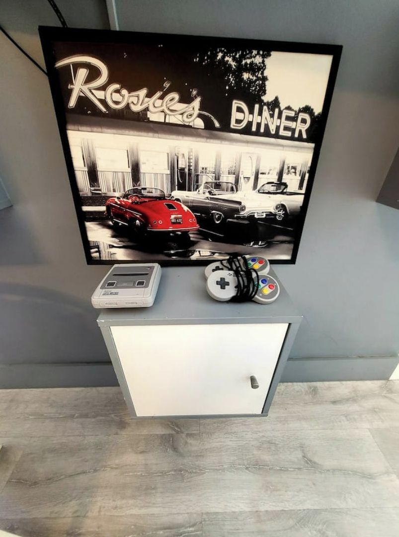 Un téléviseur à écran plat posé sur un meuble, avec une affiche sur le thème de l’automobile, une console de jeux et des manettes.