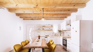 Une cuisine moderne avec des meubles blancs, un plafond en bois et un coin repas comprenant une table en bois et des chaises jaunes.