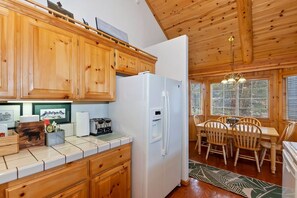 Una cocina con armarios de madera, un refrigerador blanco y una zona de comedor con mesa y sillas.