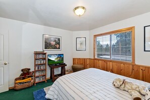 A bedroom with a bed, a television, a bookshelf, and a window.
