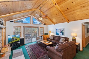 A cozy living room with a wooden ceiling, a television, a sofa, a coffee table, and a fireplace.