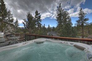 A hot tub on a deck with a view of a house and trees.