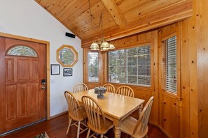 A wooden-paneled dining room with a table and chairs, a chandelier, and a large window with blinds.