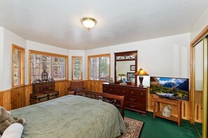 A bedroom with a bed, dresser, television, and windows.