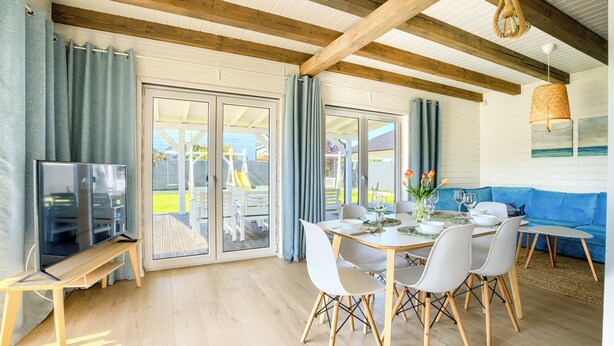 A dining area with a table set for four, white chairs, a blue sofa, and a TV on a wooden stand. - Apartamenty Sun & Snow Dom Cayetano (gmina Wolin)