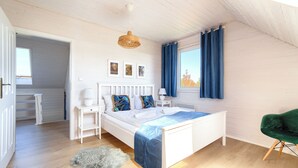 A bedroom with a white bed, a small bedside table, a green chair, and a window with blue curtains. - Apartamenty Sun & Snow Dom Cayetano (gmina Wolin)