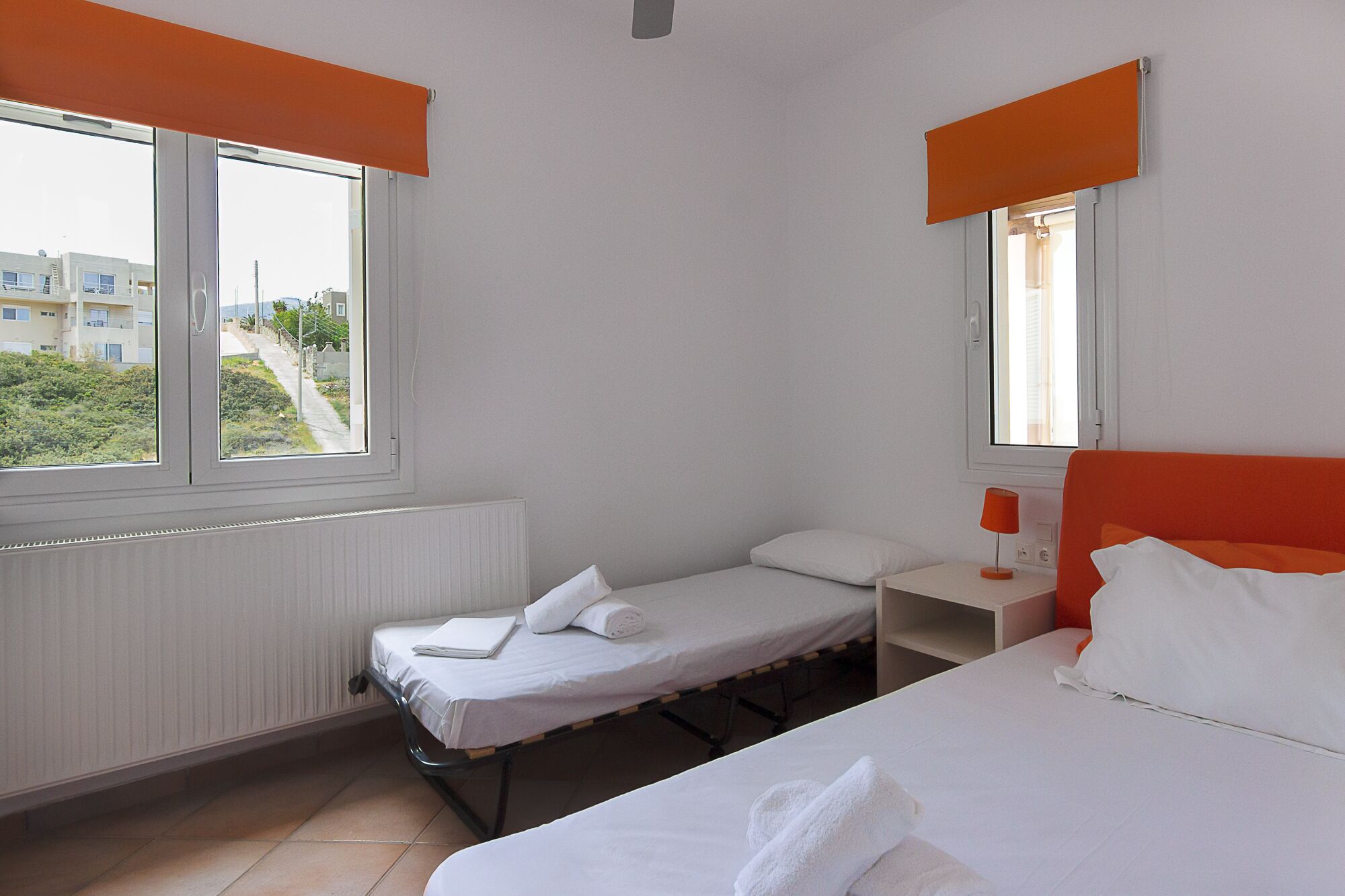 Hotellihuone, jossa on kaksi erillistä sänkyä, pieni työpöytä, tuoli ja ikkuna, josta on näkymä rakennuksiin ja viheralueille.