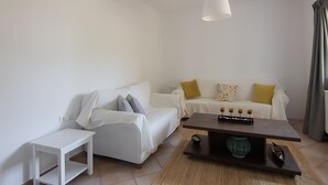 Een minimalistische woonkamer met een witte bank, een klein wit bijzettafeltje en een donker houten salontafel met decoratieve objecten.
