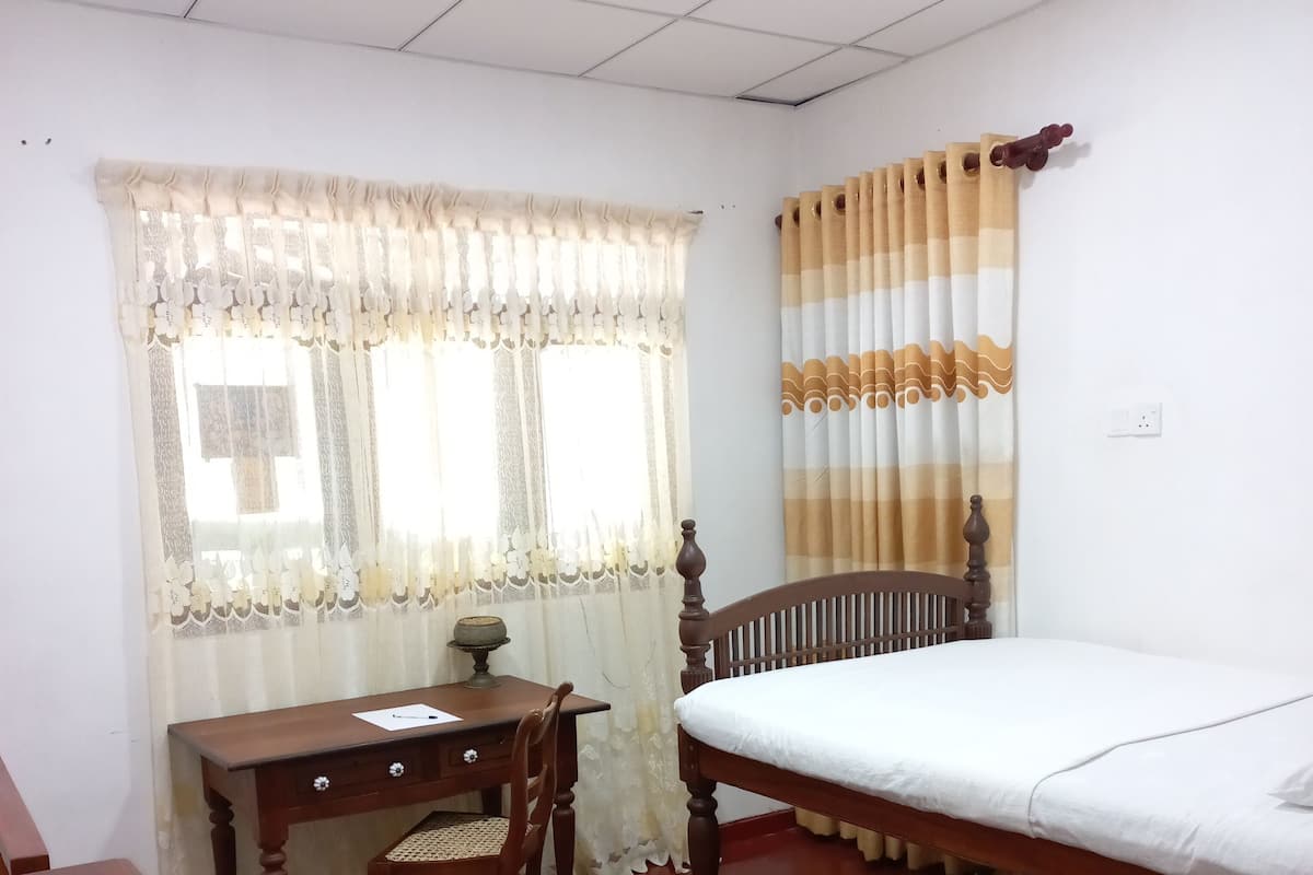 Um quarto com uma cama de madeira, uma escrivaninha com cadeira e uma janela com cortinas.