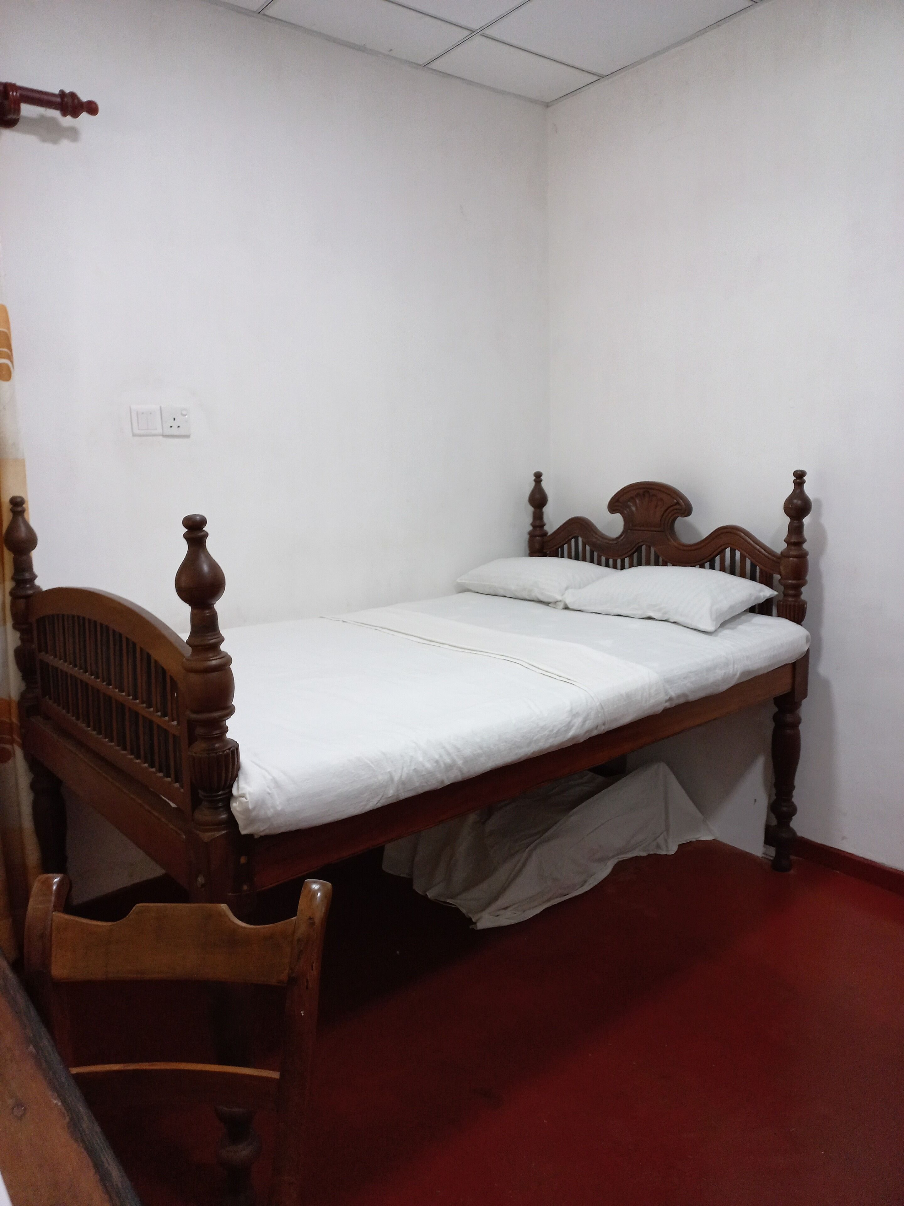 A single bed with a wooden headboard and footboard, a white mattress, and a wooden chair.