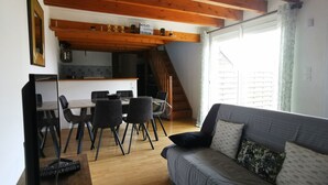 Una sala acogedora con sofá, una mesa de comedor con sillas, una zona de cocina y una escalera que sube a un piso superior.