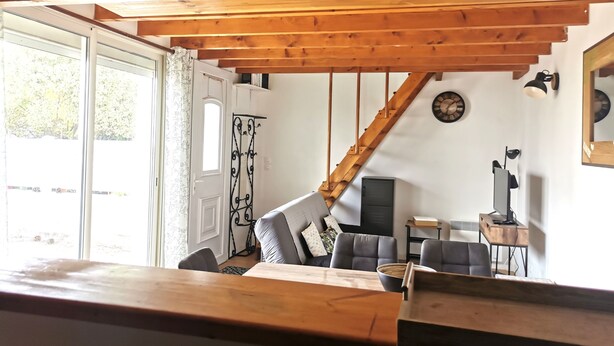 Una habitación acogedora con techo de madera, una escalera, un comedor con mesa y sillas, y un escritorio pequeño con una computadora.