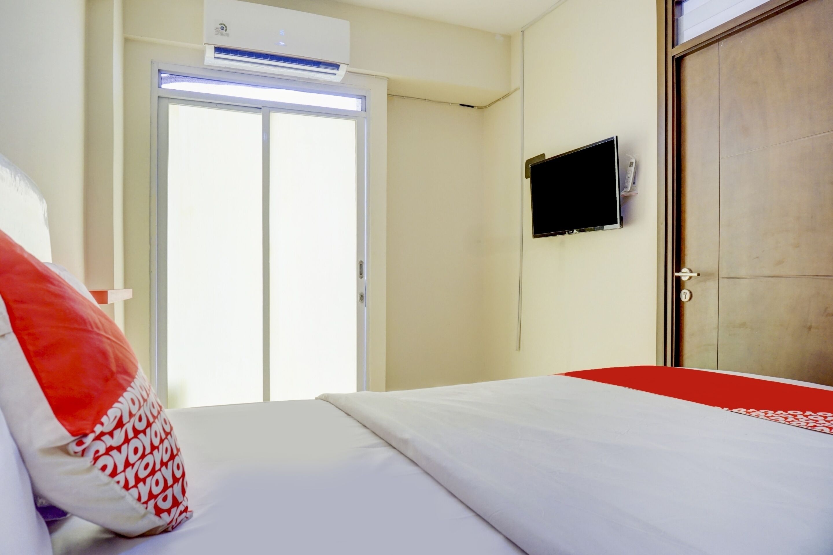 A hotel room with a bed, a television mounted on the wall, and a sliding door.