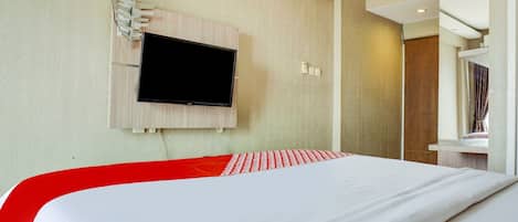 A hotel room with a bed, a mounted TV, and a wooden headboard.