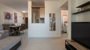 A modern living room with a sofa, dining table, and chairs. There is a TV and artwork on the walls.