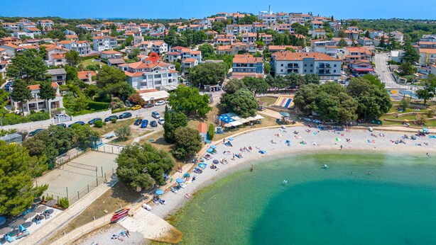 An aerial view of a coastal town with residential buildings, a sandy beach, and a clear blue sea.
