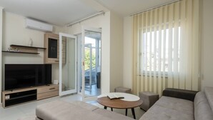 A modern living room with a flat-screen TV, a sofa, a coffee table, and a sliding glass door leading to an outdoor area.