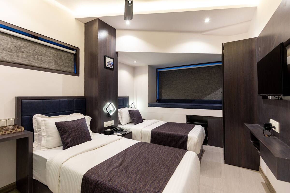 Ein modernes Hotelzimmer mit zwei Betten, einem großen Fernseher und einem Schreibtisch mit einem Computer.