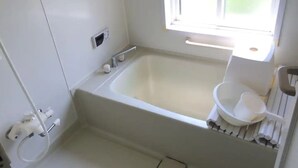 Ein kleines, weißes Badezimmer mit Badewanne, Fenster und Toilette.