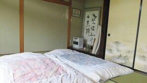 Ein traditionelles japanisches Zimmer mit Tatami-Boden, Futonbett, Shoji-Schirm und einem kleinen Heizgerät an der Seite.