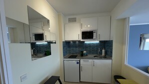 A compact kitchen with white cabinets, a microwave, and a sink. There's a small stool and a trash bin. - LLORET HIGH - PREMIUM (Lloret de mar)