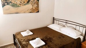 Ein Einzelbett mit brauner Bettdecke und weißen Kissen, ein Bild an der Wand und ein kleiner Nachttisch aus Holz.