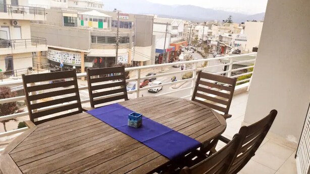 Ein Holztisch mit vier Stühlen auf einem Balkon mit Blick auf eine Stadtlandschaft, inklusive Gebäude und einer Straße.