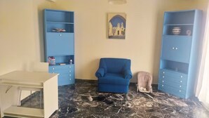 Ein Zimmer mit blauem Sessel, einem kleinen Tisch und zwei blauen Regale an der Wand.