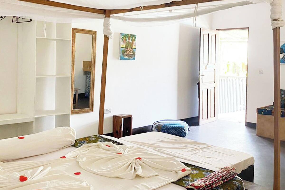 A room with a bed, a mirror, a small table, and a door leading to another room.