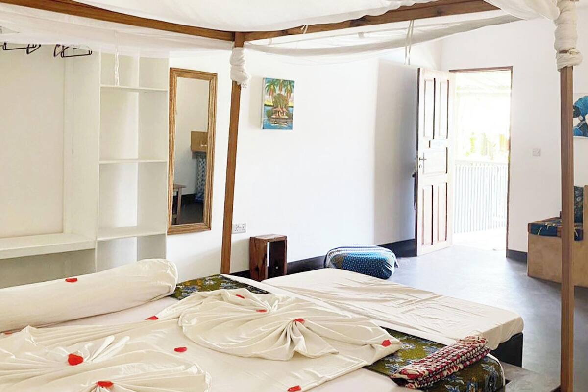 A room with a bed, a mirror, a small table, and a door leading to another room.