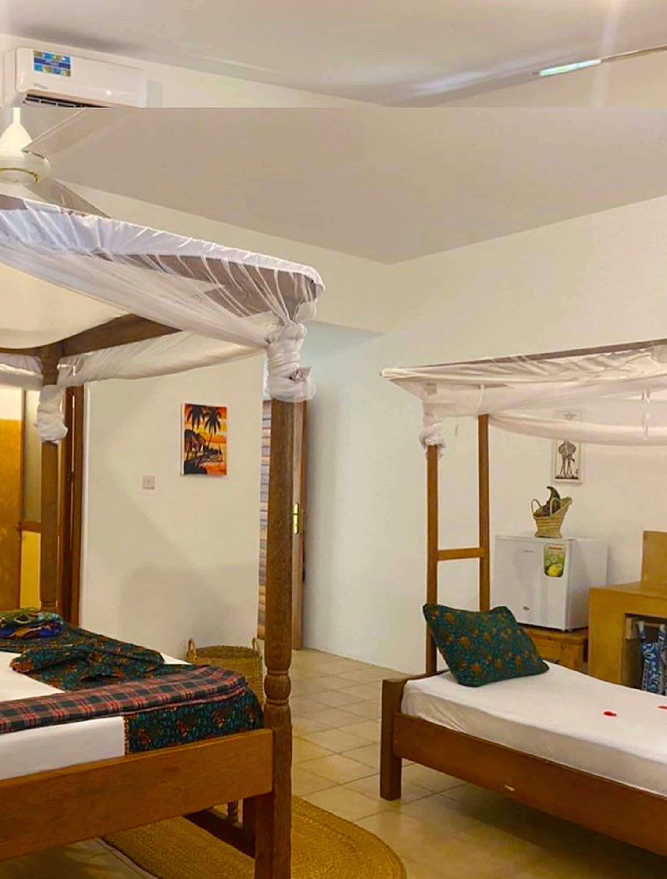 A room with two wooden beds, each with a canopy, a small table, and a refrigerator.