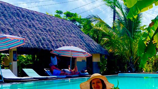 A pool area with lounge chairs and umbrellas, a thatched-roof structure, and tropical vegetation. - Shamba Village Hotel (Paje)