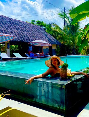 A pool area with lounge chairs and umbrellas, a thatched-roof structure, and tropical vegetation. - Shamba Village Hotel (Paje)