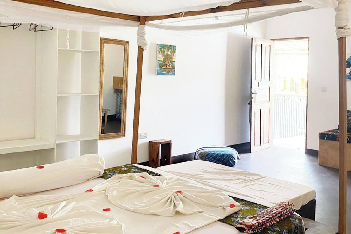 A room with a bed, a mirror, a small table, and a door leading to another room.