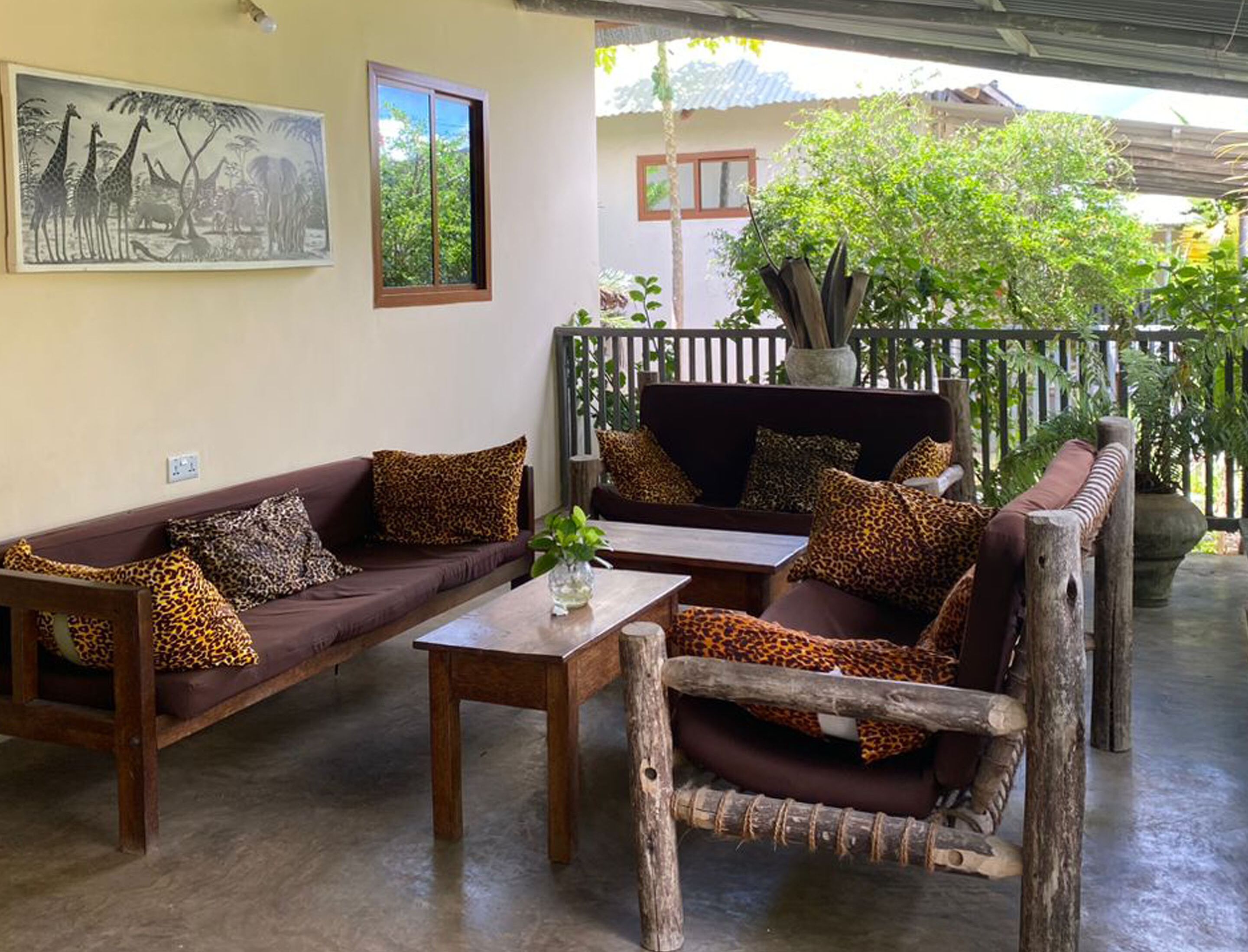 A cozy outdoor seating area with two sofas and a table, surrounded by lush greenery and a wooden fence.