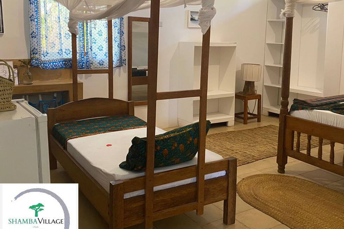 A room with a four-poster bed, a small desk, a chair, a shelf, and a wardrobe.