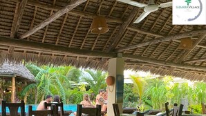 An outdoor dining area with thatched roofs and wooden tables and chairs. - Shamba Village Hotel (Paje)