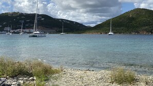 A coastal scene with boats on calm water, rocky shore, and hills in the background. - Oceanfront Beach Luxury Retreat (St Thomas)