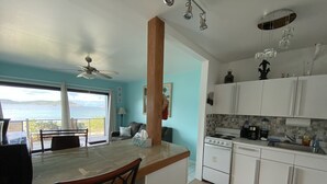 A kitchen with a view of the sea, a dining area with a table and chairs, and a ceiling fan. - Oceanfront Beach Luxury Retreat (St Thomas)